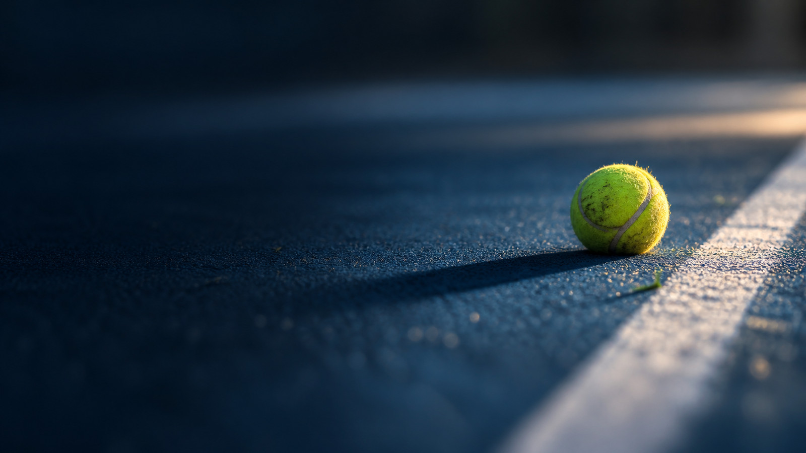 A tennis ball on the line of an empty court at dusk, the draw not yet played.